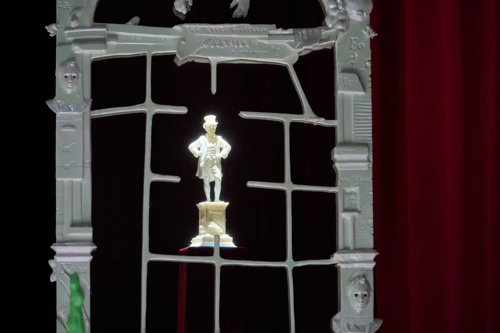 A white figurine standing inside a grey window-like sculpture in the FACT gallery