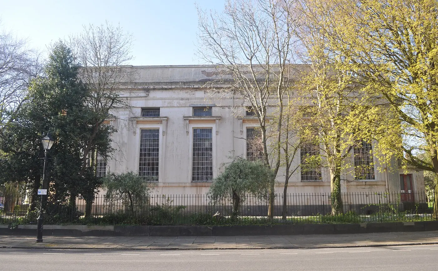 The pale stone neoclassical front of St Bride's Church behind trees and railings